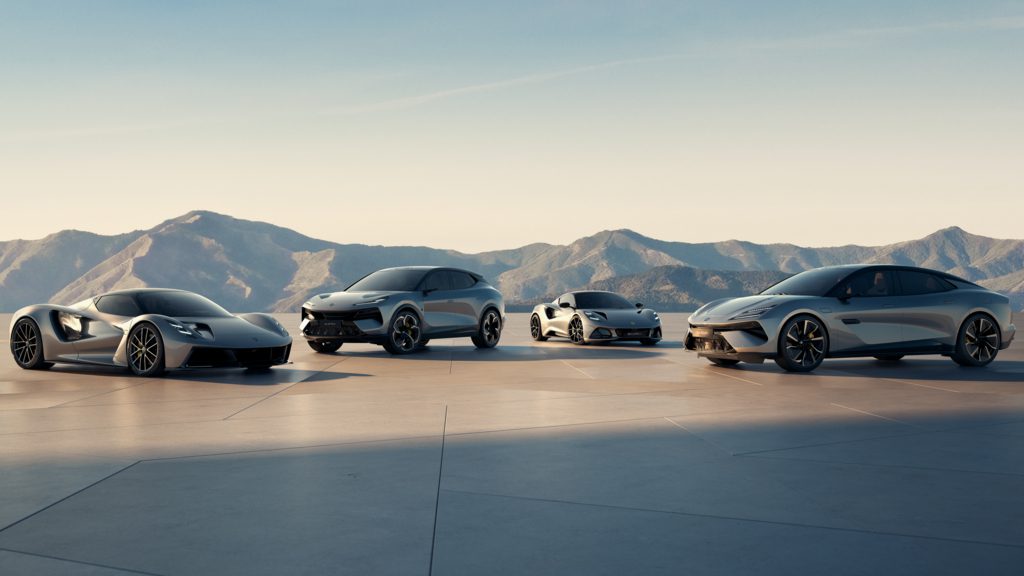 Four modern silver sports cars are parked side by side on a flat surface with mountains and a clear sky in the background.