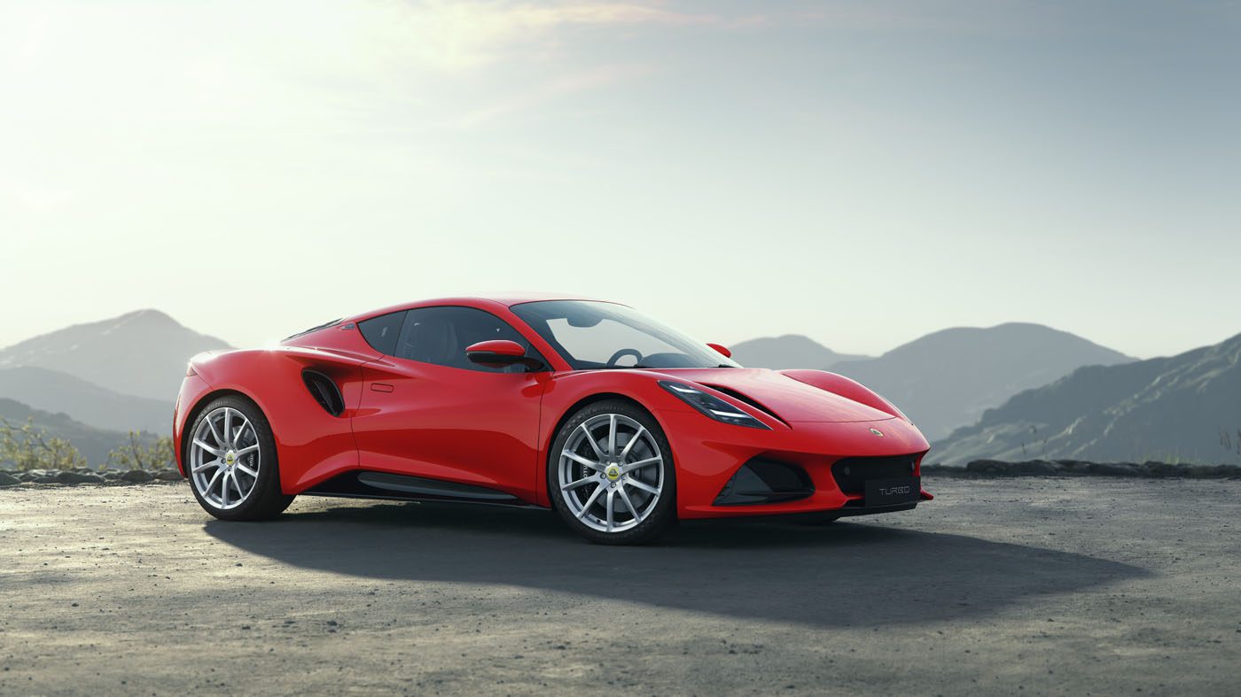 A sleek red sports car, the Lotus Emira Turbo, rests on a paved surface with majestic mountains in the backdrop under a clear sky, boasting an impressive 400HP.