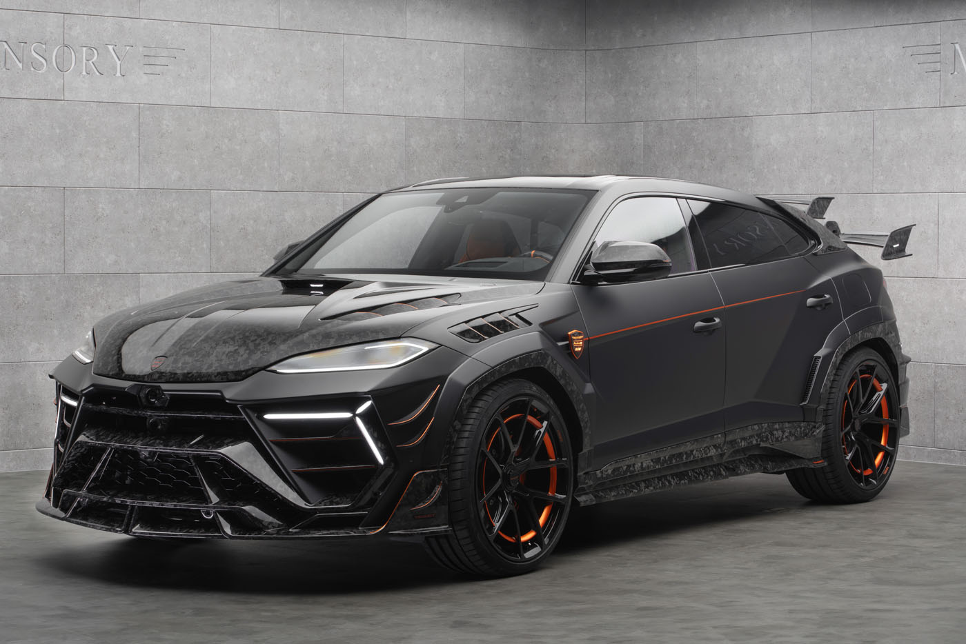 A black Lamborghini Urus SUV with orange accents and a custom Mansory body kit is parked in a modern, gray-tiled showroom.