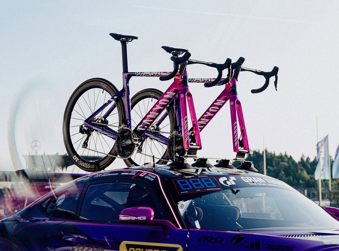 Two purple Canyon Aeroad Road Bikes are mounted on the roof rack of a parked Mercedes-AMG sports car at an outdoor event.