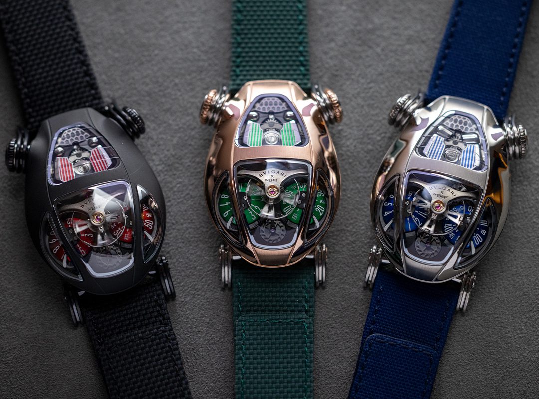 Three unique car-shaped wristwatches, reminiscent of MB&F's avant-garde designs, with visible gears on black, green, and blue straps are displayed on a gray surface.