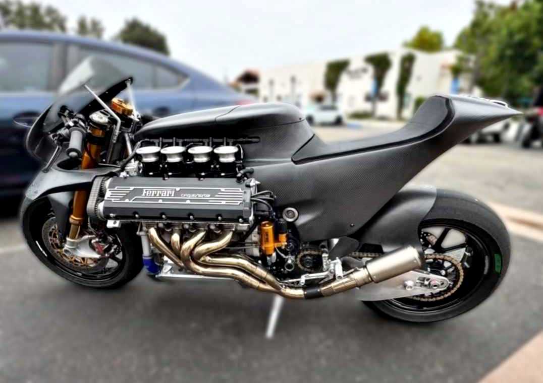 A bespoke superbike with a massive exposed Ferrari V8 engine stands parked outdoors on two wheels, surrounded by cars and buildings in the background.