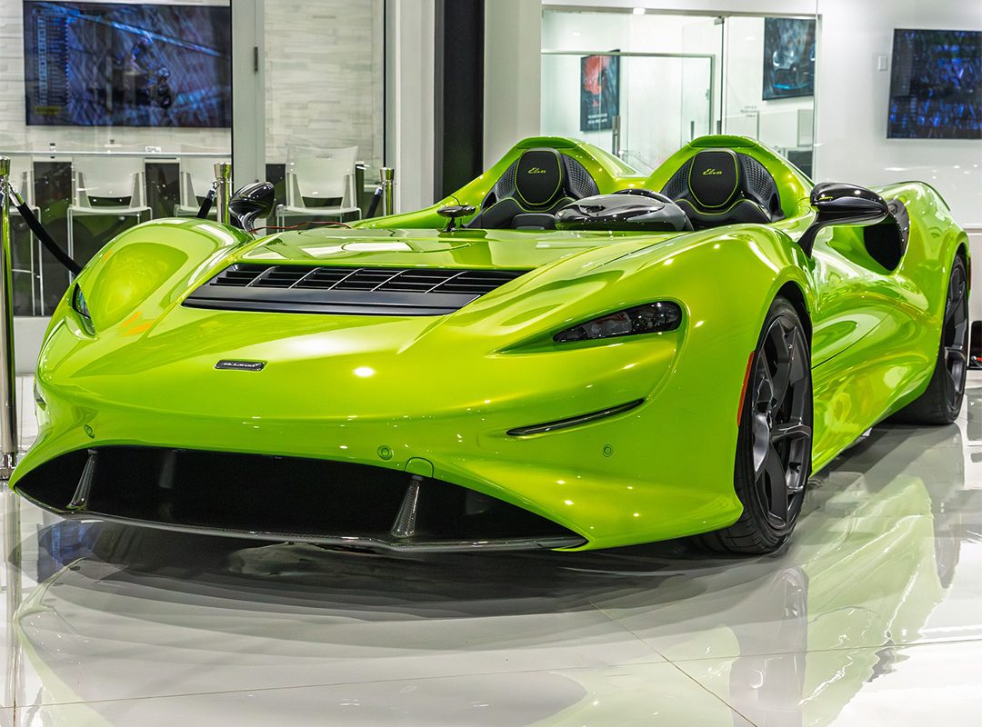 A bright green McLaren Elva, one of the most expensive McLarens, is displayed indoors on a glossy floor—an iconic example of luxury sports cars with no windshield.
