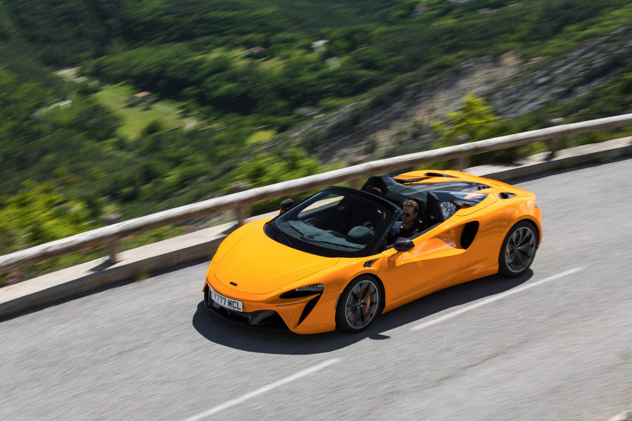 An image of a McLaren Artura Spider driving on a mountain road.