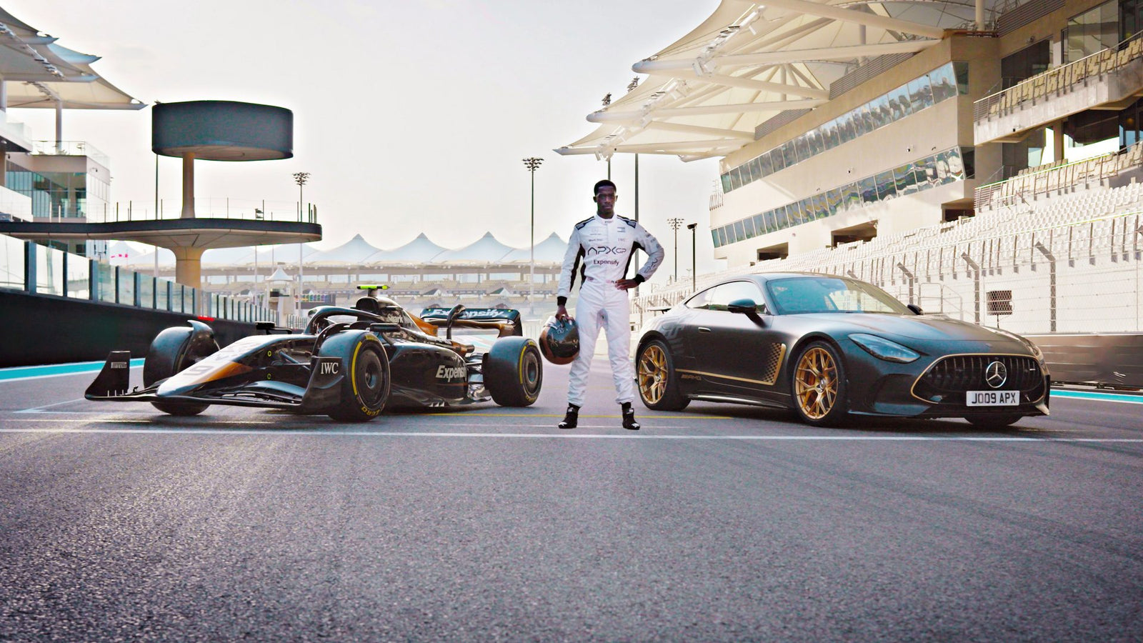 A person in a racing suit stands between a Formula 1 car and a limited-run Mercedes-AMG GT 63 on a racetrack with grandstands in the background, evoking scenes from the upcoming Brad Pitt F1 film.