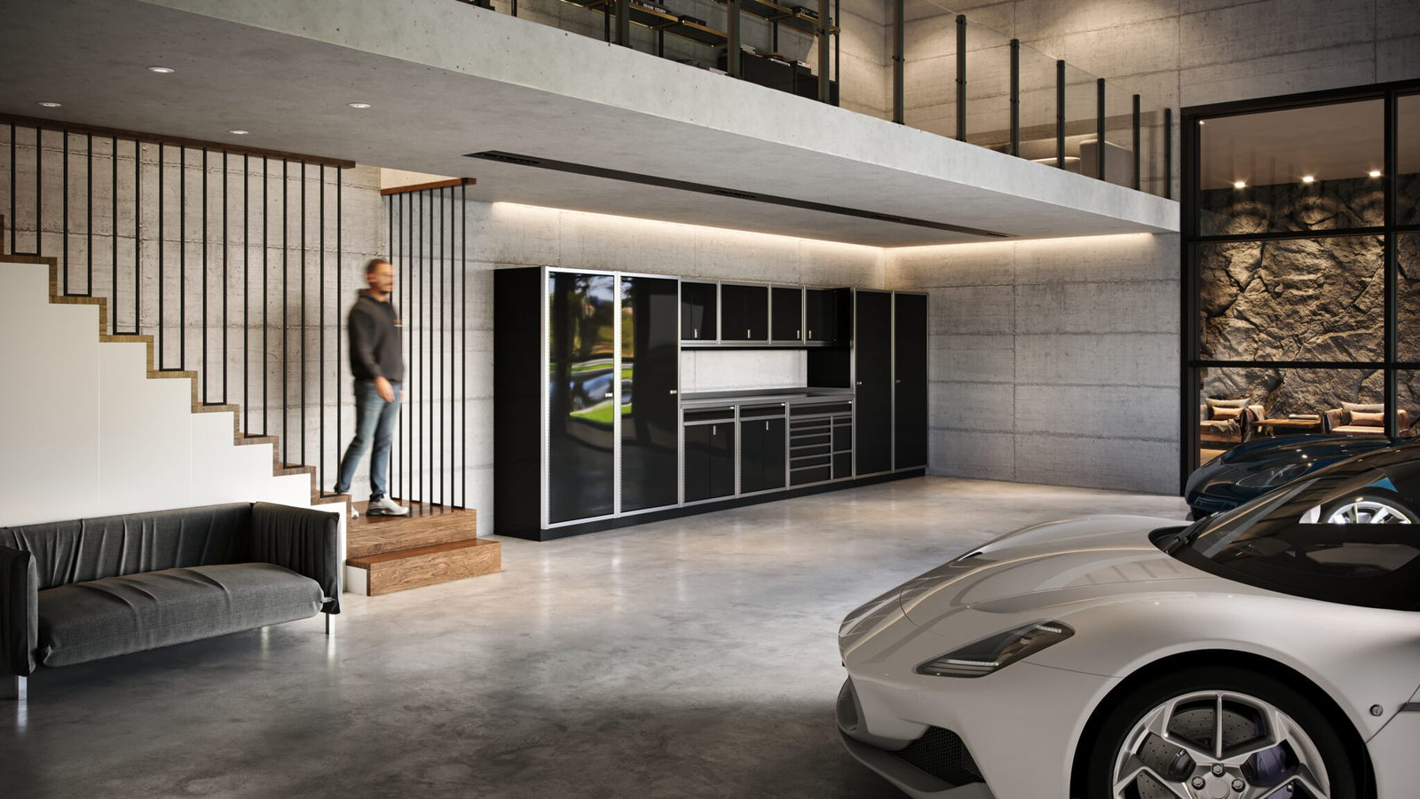 A man descends stairs into a modern garage with concrete walls, a black sofa, a kitchen area, and two parked sports cars—an impressive space that reflects refined living and luxury home accessories.