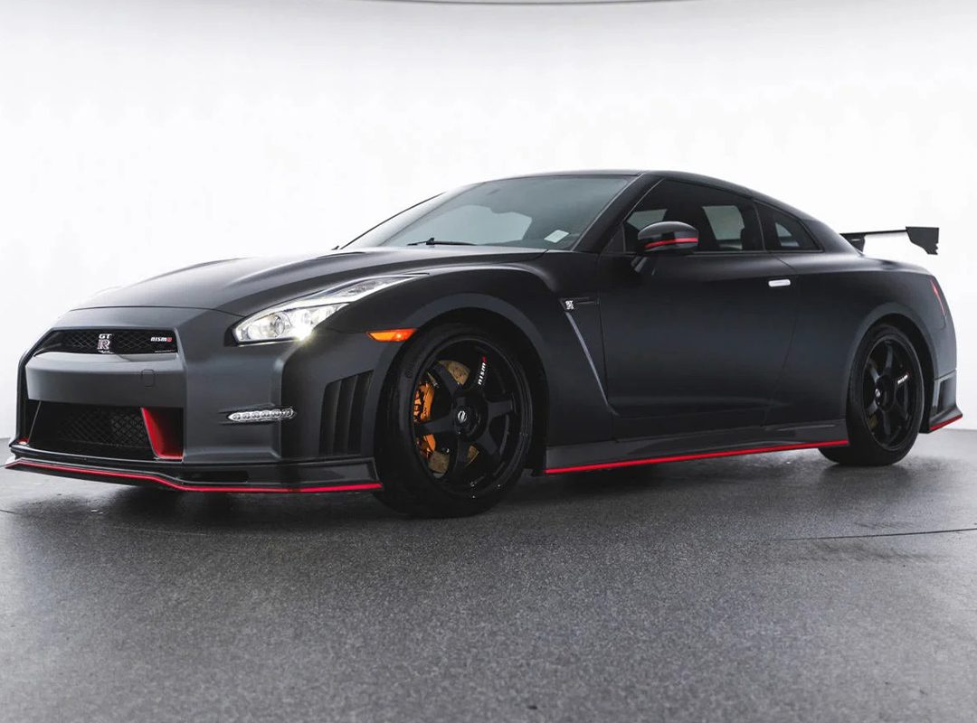 A black Nissan GT-R sports car with red accents and a rear wing is parked in a plain indoor setting, featured as part of the dealer spotlight at OpenRoad Northwest—your destination for exotics for sale.