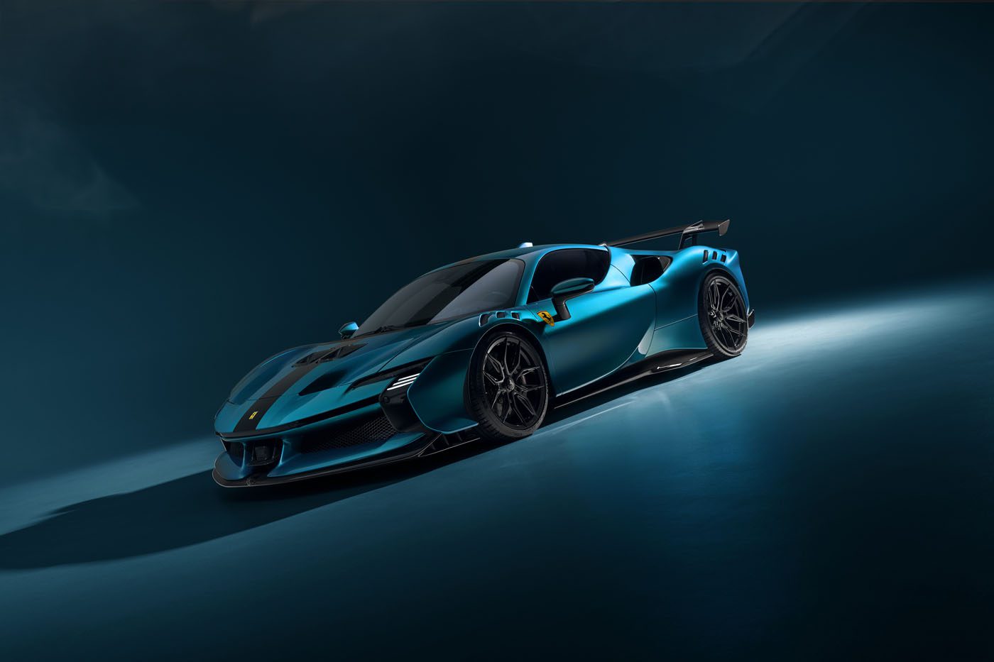 A blue Ferrari SF90 XX Stradale with NOVITEC customizations and black accents stands on a smooth surface, its large rear wing catching dramatic, low lighting—a striking example of Ferrari tuning at its finest.