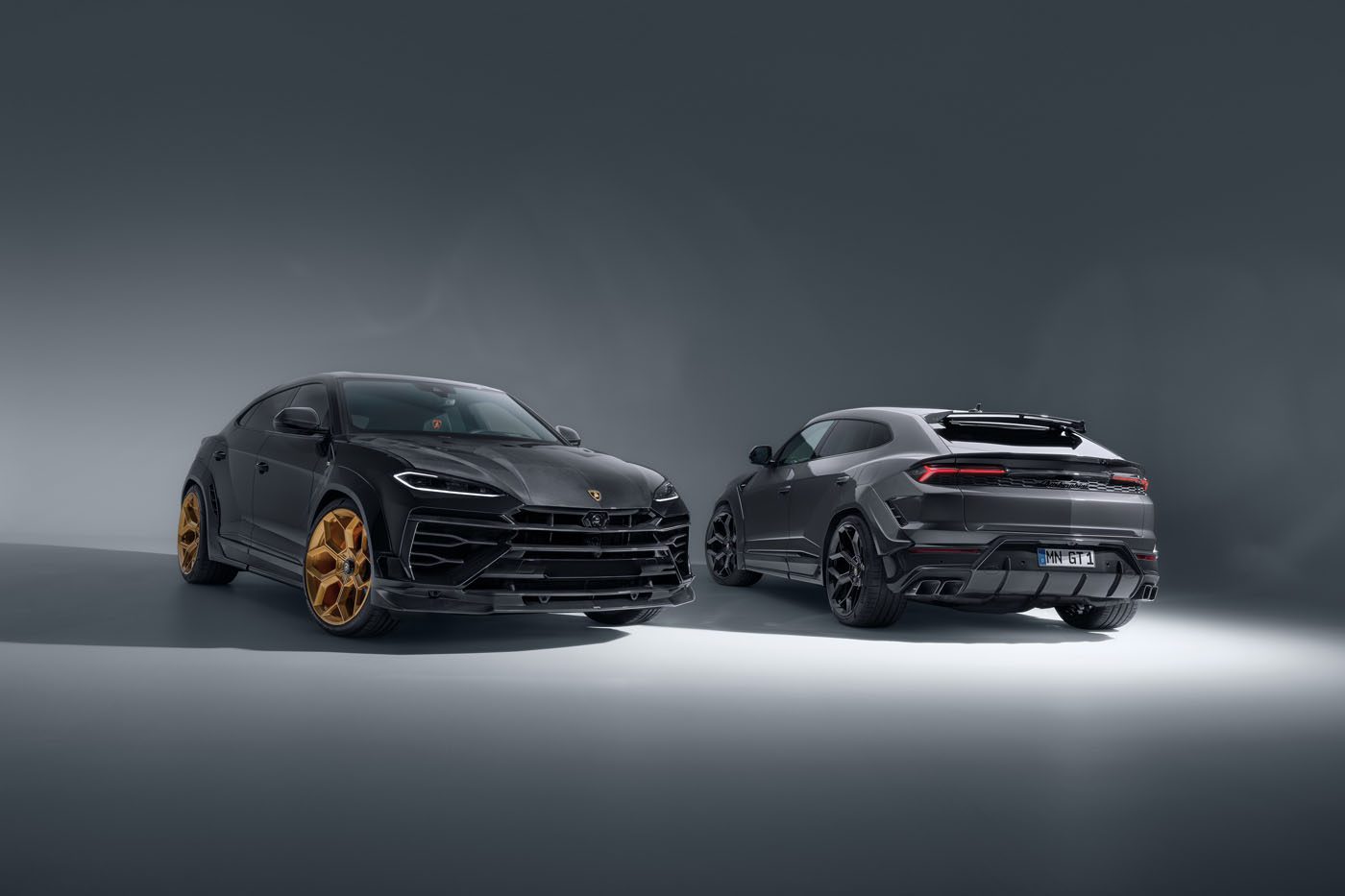 Two Lamborghini Urus SUVs are displayed in a studio; one faces front with gold wheels, the other shows the rear view with black wheels.