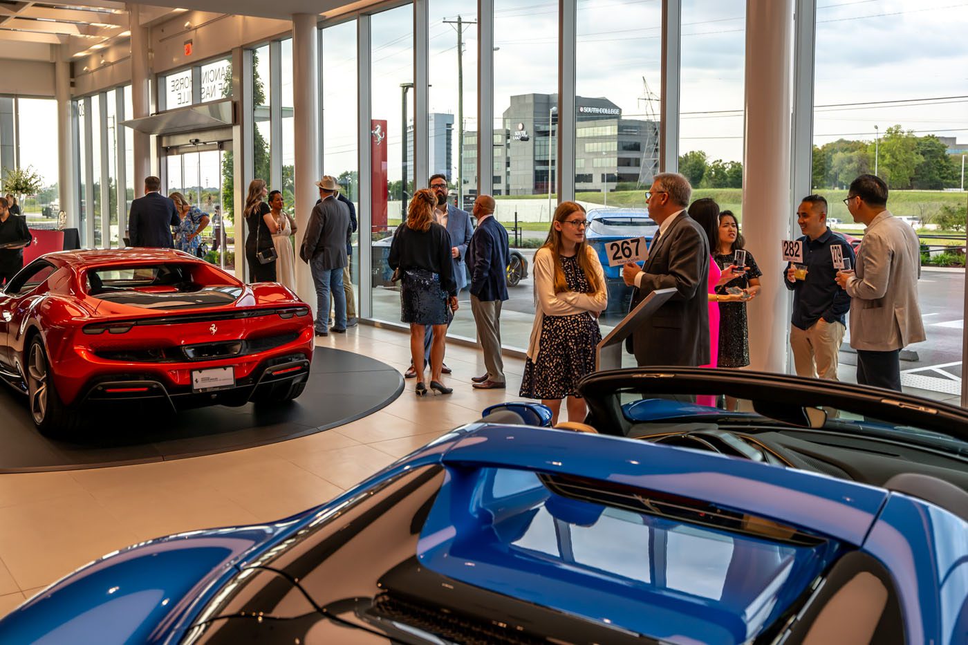 At the Middle Tennessee Gala, people converse at a car dealership event, surrounded by luxury cars. Indoors, natural light from large windows highlights a night where dreams come true.