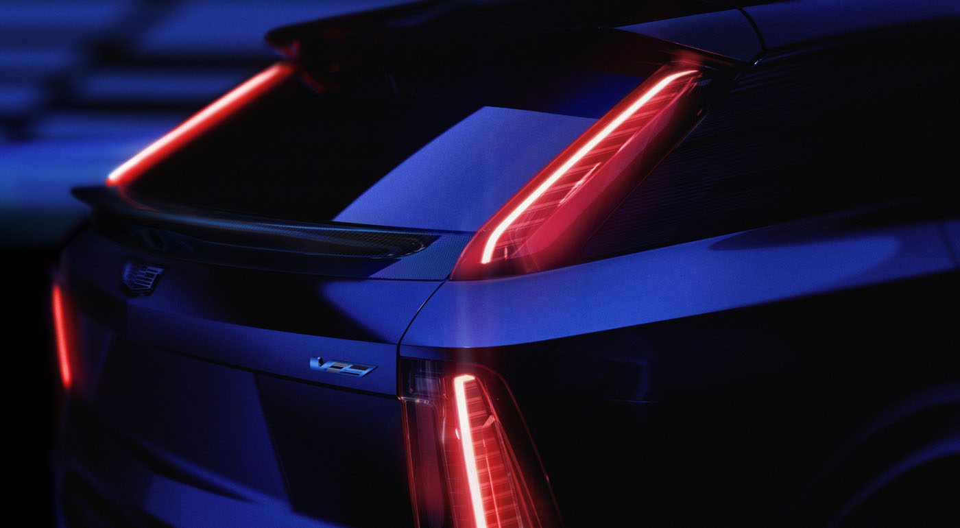 Close-up of the rear end of a dark blue 2026 Optiq-V Cadillac SUV with vertical LED taillights illuminated and a V-series badge visible.