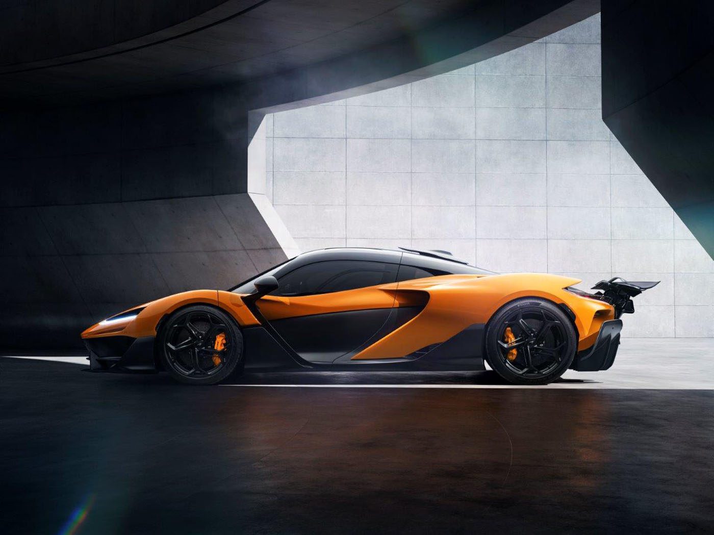 Orange and black McLaren W1 sports car parked in a modern, minimalistic concrete setting with indirect sunlight highlighting its sleek design and Pirelli bio-based tires.