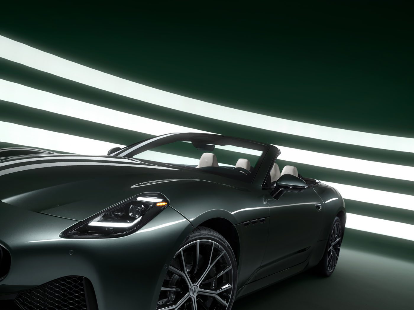 A sleek, dark green Maserati GranCabrio with its top down is parked in a futuristic, illuminated tunnel-like setting, exuding an air of I.C.E. St. Moritz sophistication and style.