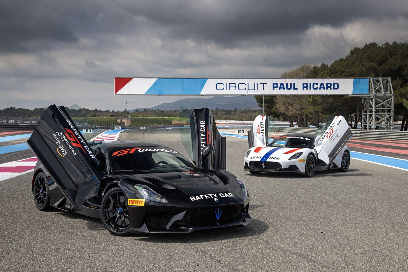 Two sports cars with open scissor doors are parked on the racetrack at Circuit Paul Ricard. One, a Maserati GT2 Stradale, is labeled as a safety car, setting the scene for an exhilarating event in the GT World Challenge Europe.