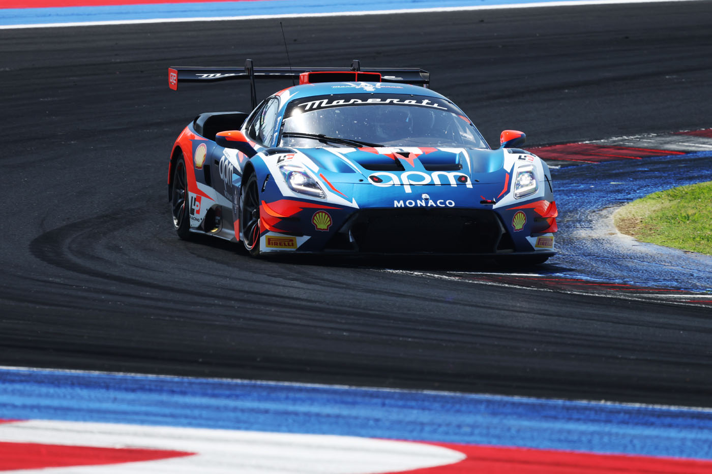 A blue, red, and black Maserati race car speeds around a bend at Misano racetrack, with Shell and Monaco sponsor logos visible.