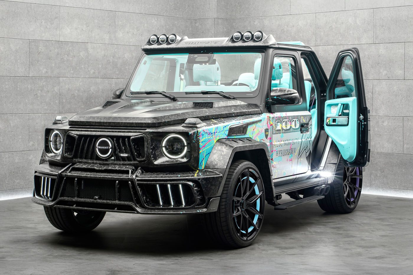 A customized Mansory G-Wagon with a carbon fiber body, colorful graphic accents, black wheels, and a turquoise interior, parked indoors with the driver's door open.