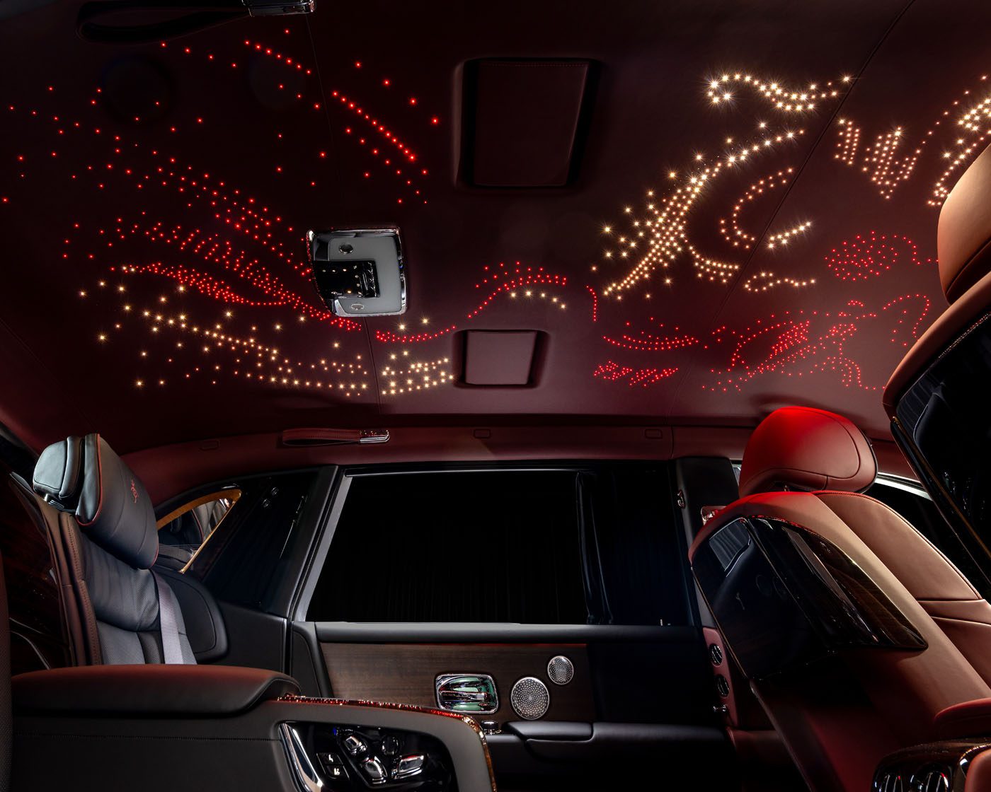 Experience the bespoke luxury of a Rolls-Royce interior, where an illuminated ceiling dazzles with star-like and abstract patterns in red and white, creating an ethereal ambiance.