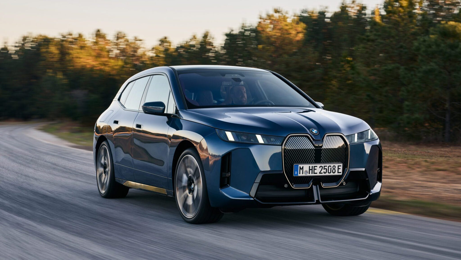 A blue BMW electric SUV driving on a road with blurred background trees.