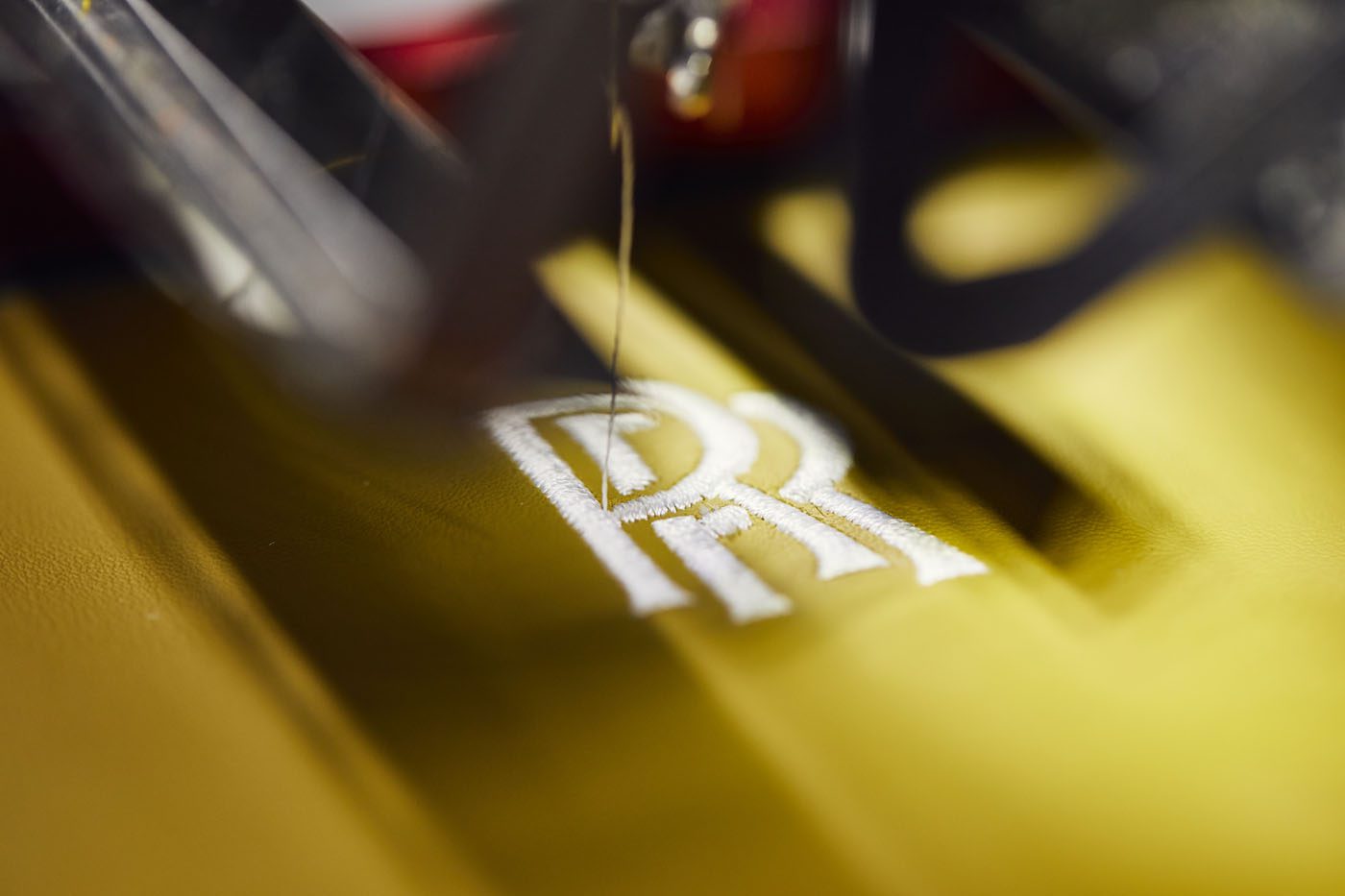 Close-up of a sewing machine embroidering the opulent "RR" initials on yellow fabric, reminiscent of the craftsmanship found in a luxury Rolls-Royce.