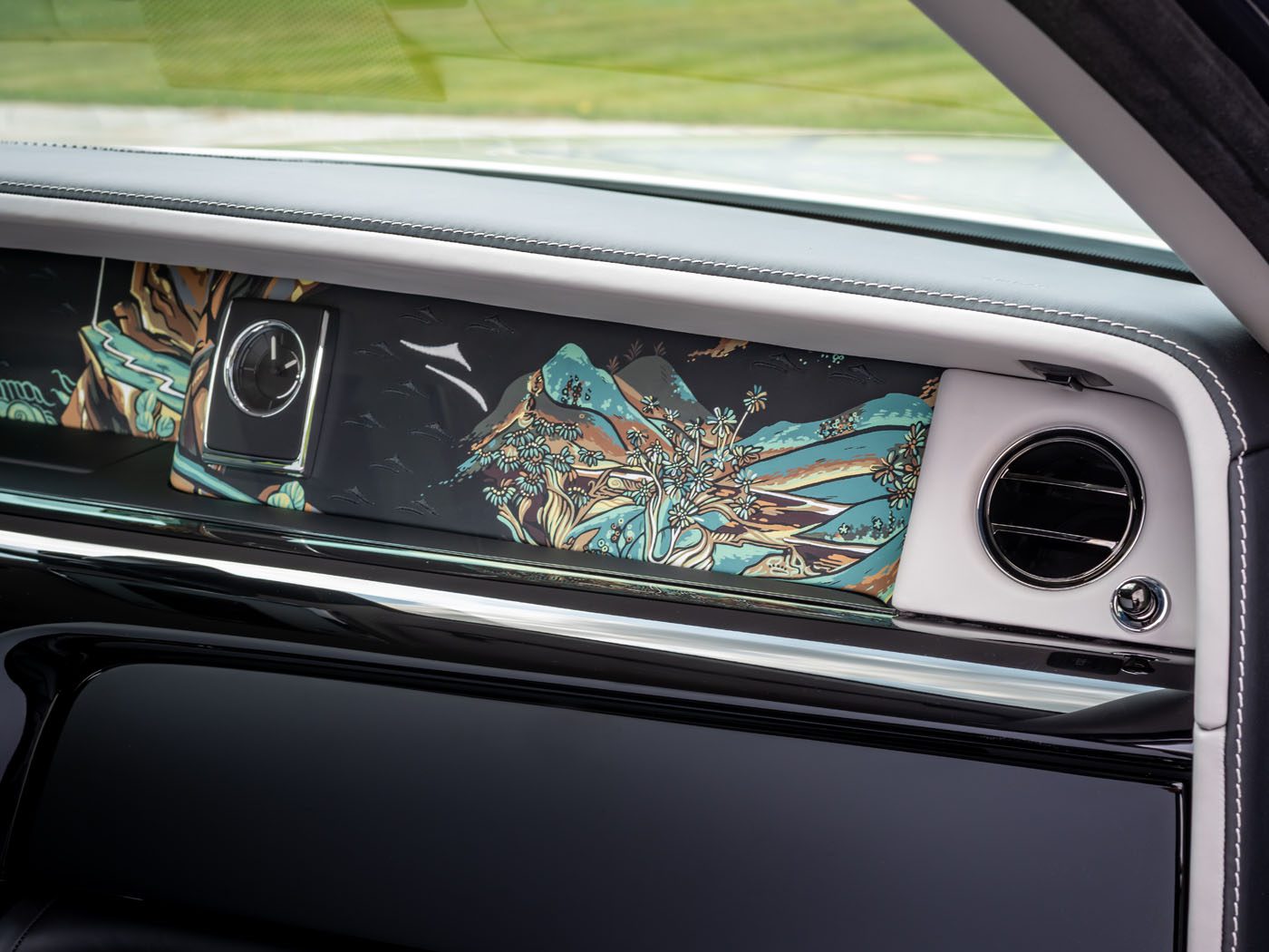 Close-up of a Rolls-Royce dashboard featuring a clock, air vent, and decorative panel with a colorful landscape inspired by bespoke Chinese murals of mountains and trees.