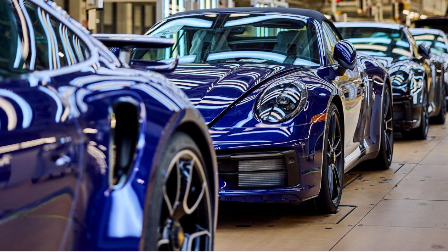 A line of sleek blue sports cars, resembling Porsche models known for record sales in the U.S., gleams in the factory setting with prominent reflections and elegant design.