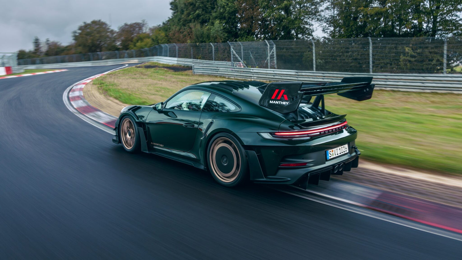 A dark green Porsche 911 GT3 RS roars down a wet U.S. racetrack, leaving a blur of trees in its wake.