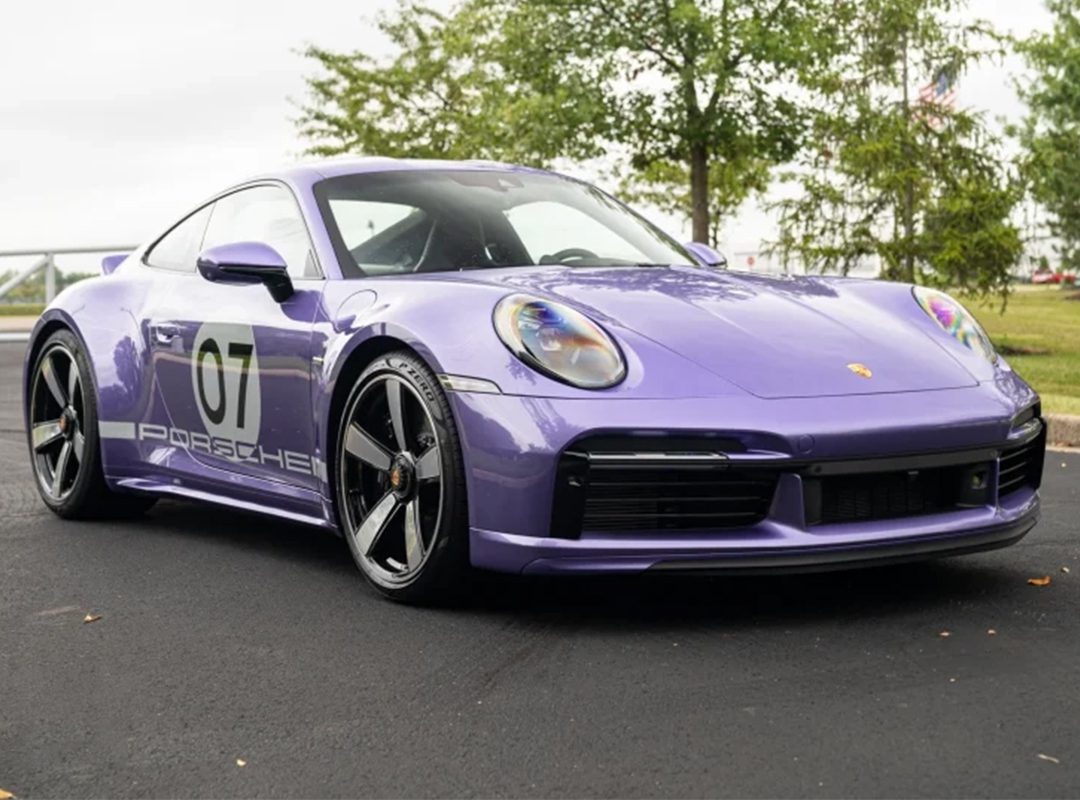 A metallic purple Porsche 911 Sport Classic, marked with the number 07 on its side, sits parked on a paved surface with trees in the background.