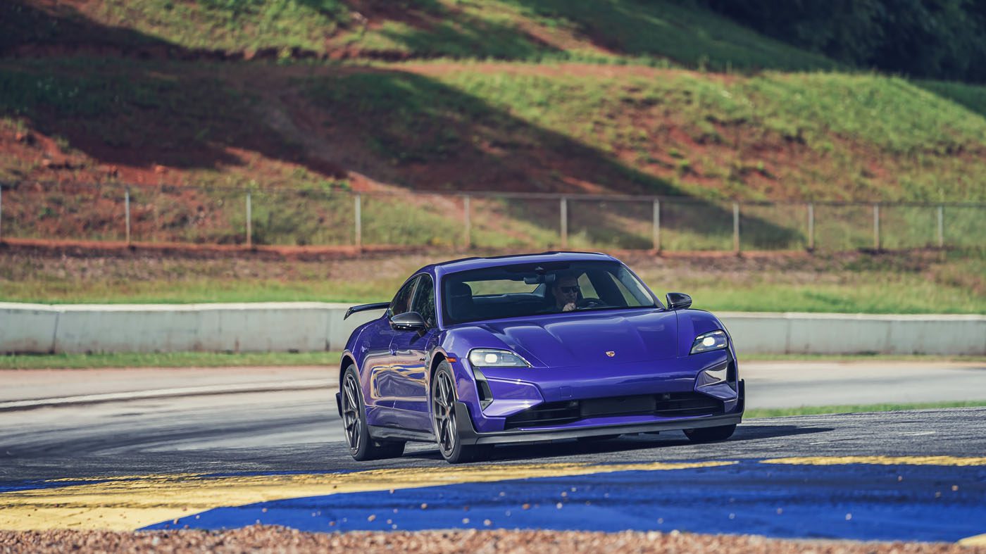 A purple Porsche Taycan Turbo GT drives on a racetrack at Road Atlanta, setting its sights on the EV Lap Record amid grass, fencing, and a hillside backdrop.