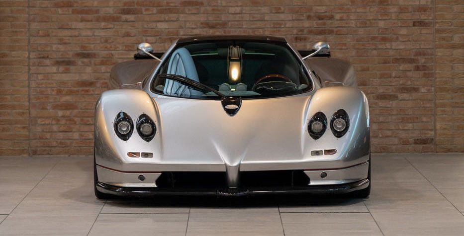 Front view of a sleek, silver Utopia Roadster with four headlights, parked indoors in front of a brick wall, echoing the elegance found at Pagani Displays.