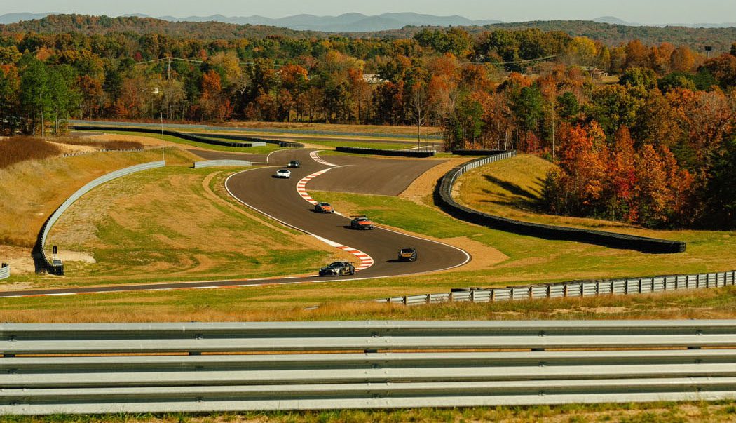Cars driving on a curvy racetrack at Flatrock Motorclub's Club Circuit, surrounded by autumn foliage and distant hills, perfectly capture the excitement of its grand opening.