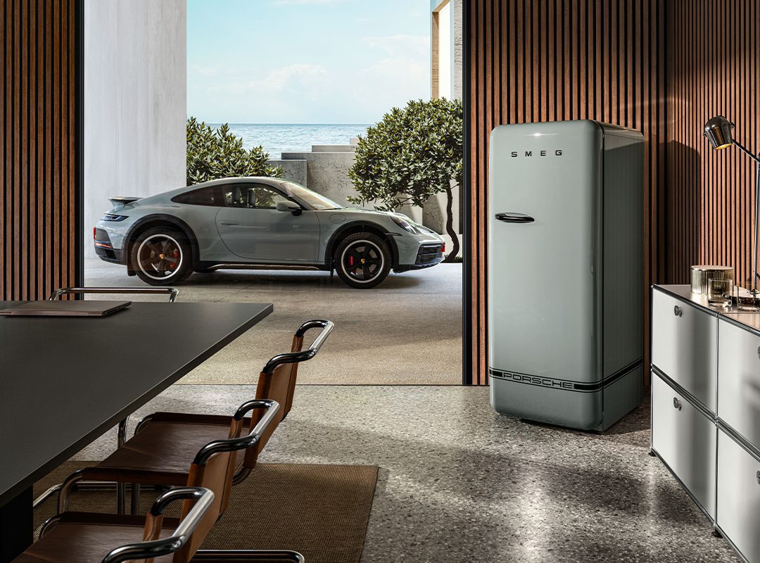 A modern kitchen with a retro-style SMEG refrigerator showcases a perfect collaboration of classic design, while a sleek Porsche sports car is parked outside near the ocean.