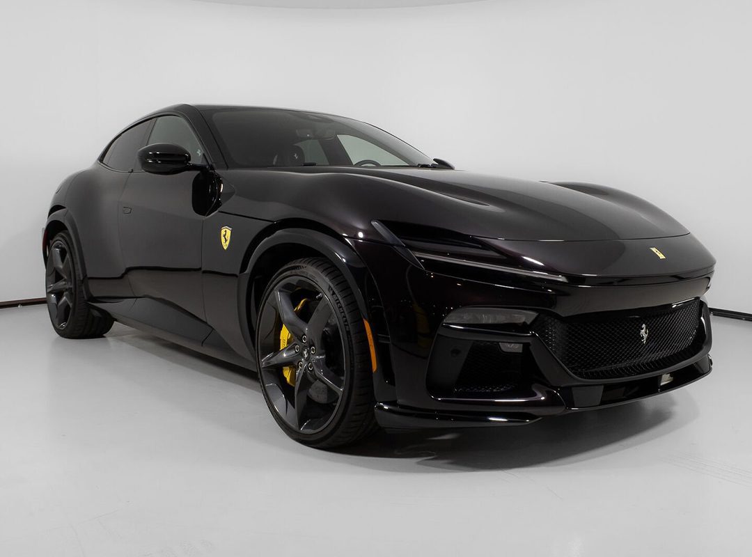 A sleek black sports car, part of the exclusive Wheels x Wardrobe collection, features striking yellow brake calipers as it sits elegantly in a well-lit, plain white room.