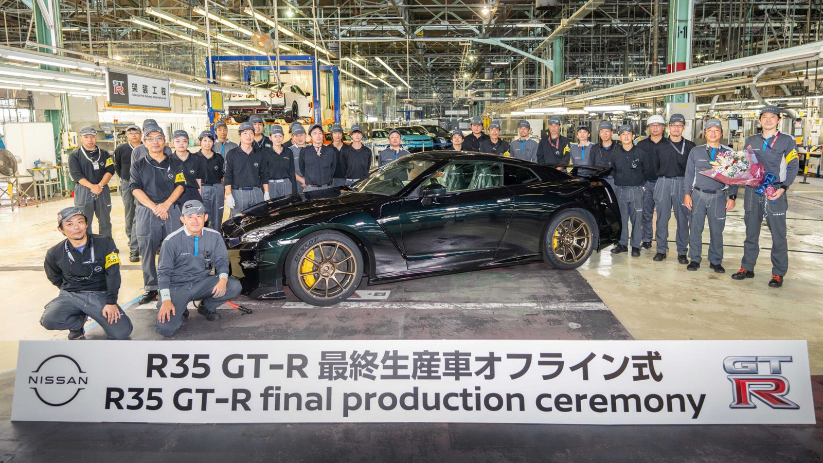 A group of factory workers poses with the last Nissan R35 GT-R beside a sign reading "R35 GT-R final production ceremony," marking the end of an era inside an automotive assembly plant.