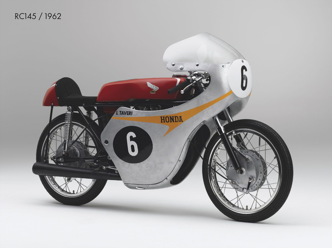 Side view of a 1962 Honda RC145 racing motorcycle with number 6 on its fairing, silver and red bodywork, and "HONDA" branding.