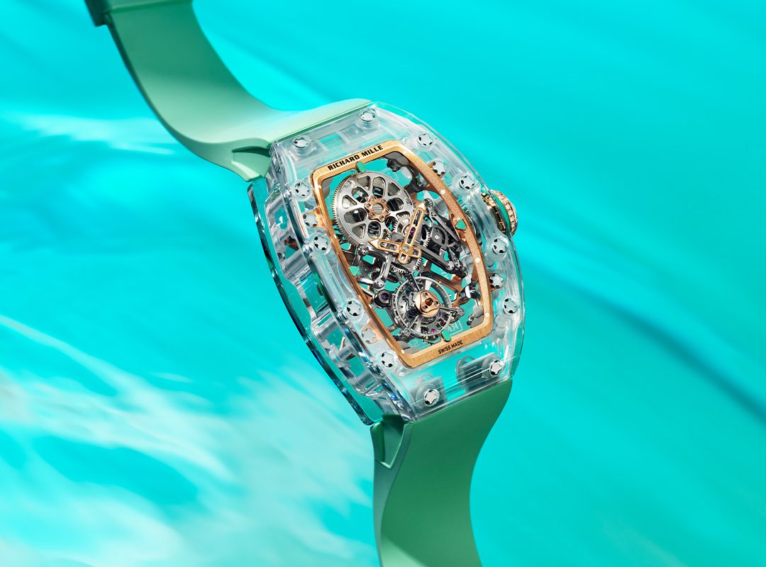 A close-up of a transparent Richard Mille RM 75-01 mechanical wristwatch with a green strap, floating above a turquoise water background—part of the stunning Sapphire Collection.