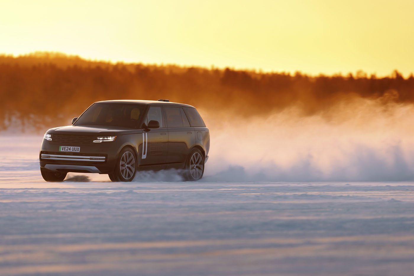 A black Range Rover Electric drives across a snow-covered landscape in Sweden at sunset, kicking up a cloud of snow behind it during cold weather testing.