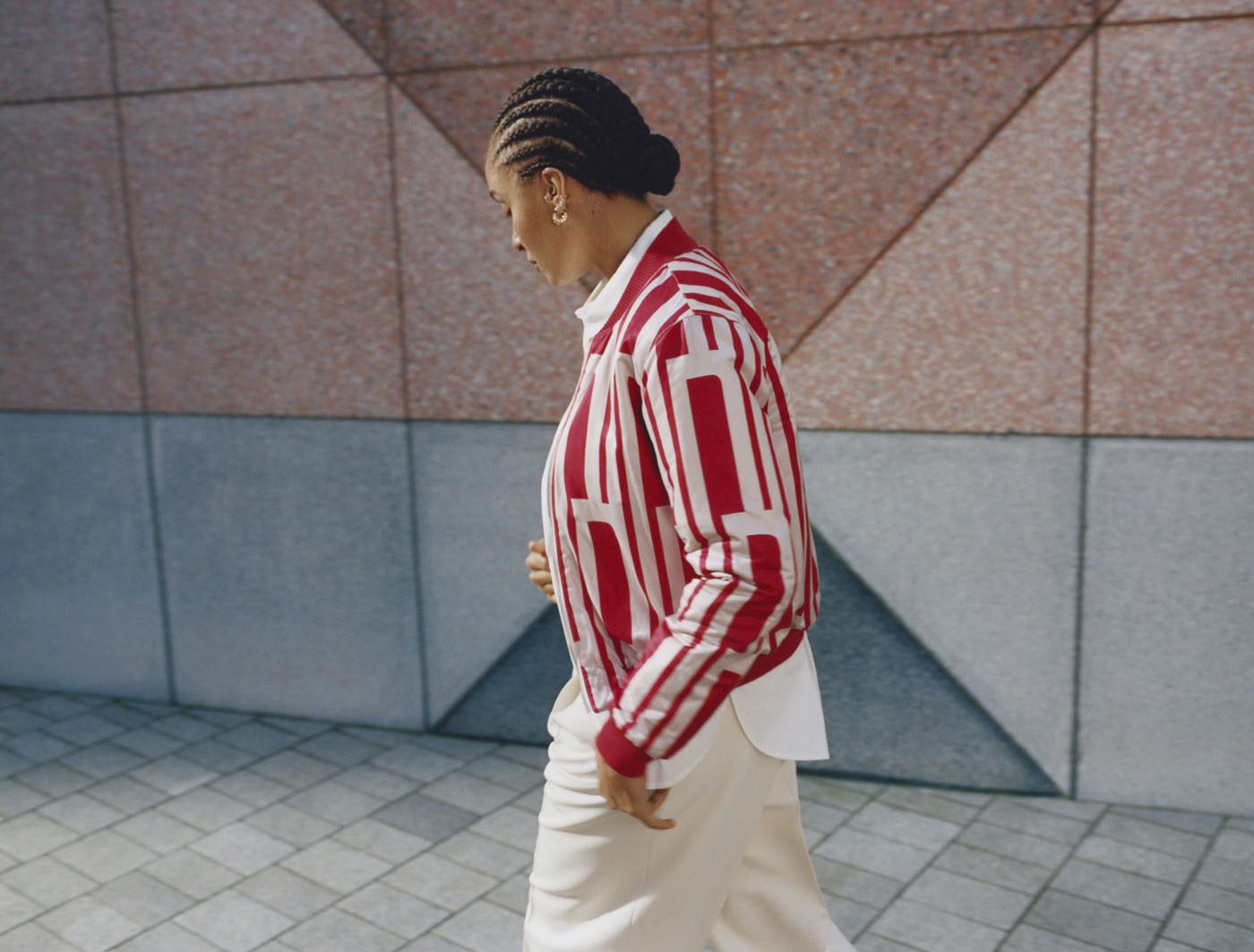 Person in a striped red and white jacket walks on tiled pavement with a geometric wall background.