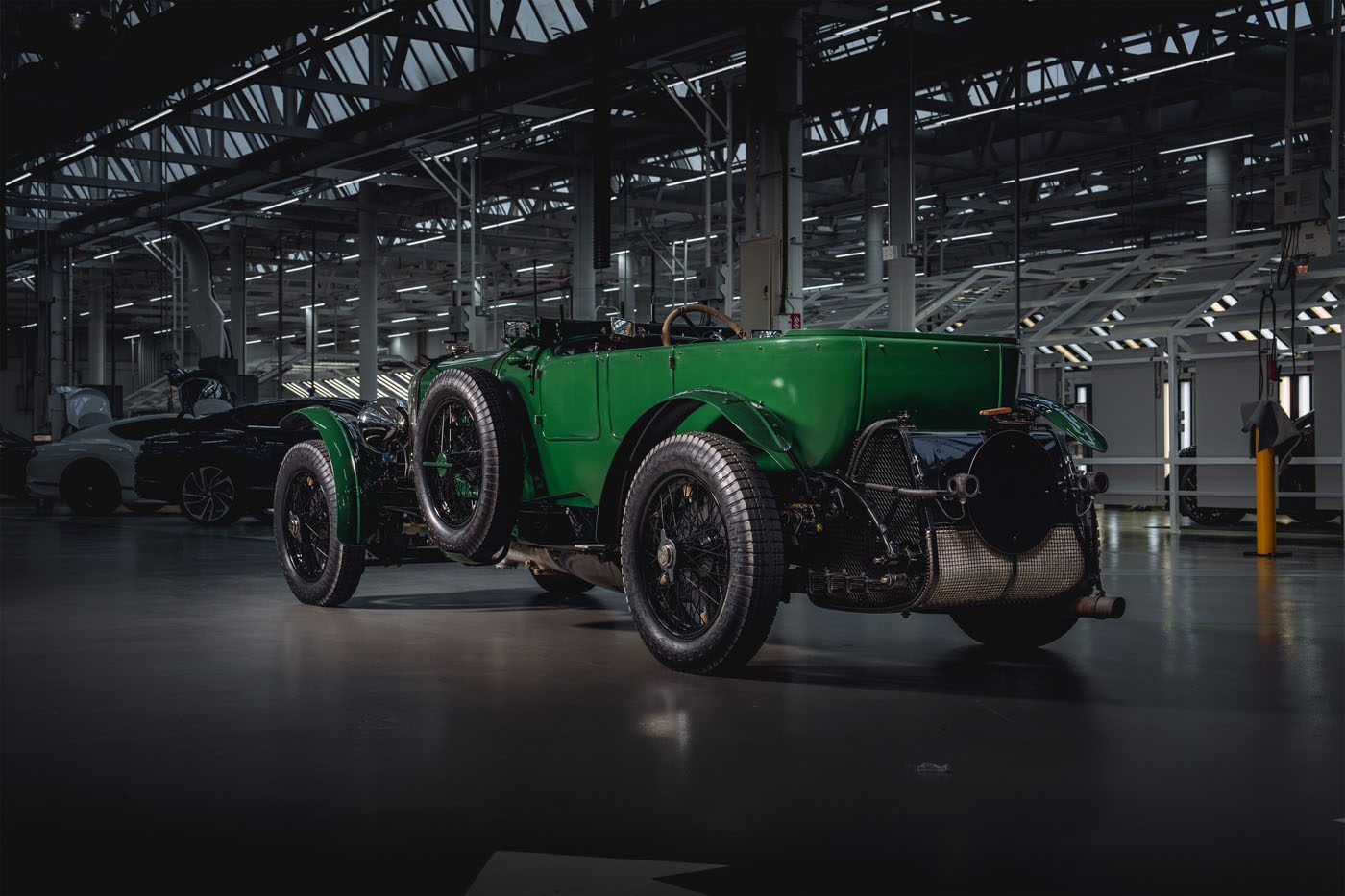 A vintage green Bentley, reminiscent of the classic Speed Six, is parked indoors. It proudly showcases its timeless design with large wheels and exposed mechanical components, echoing an era of elegance and performance.