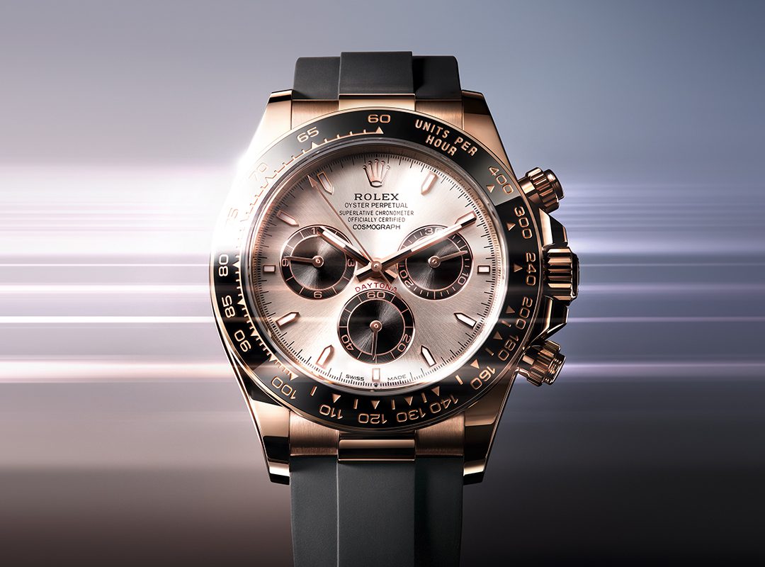 A Rolex Oyster Perpetual Cosmograph Daytona, one of the most iconic luxury chronographs, featuring a rose gold case, black bezel, and black rubber strap set against a blurred gradient background that evokes automotive elegance.