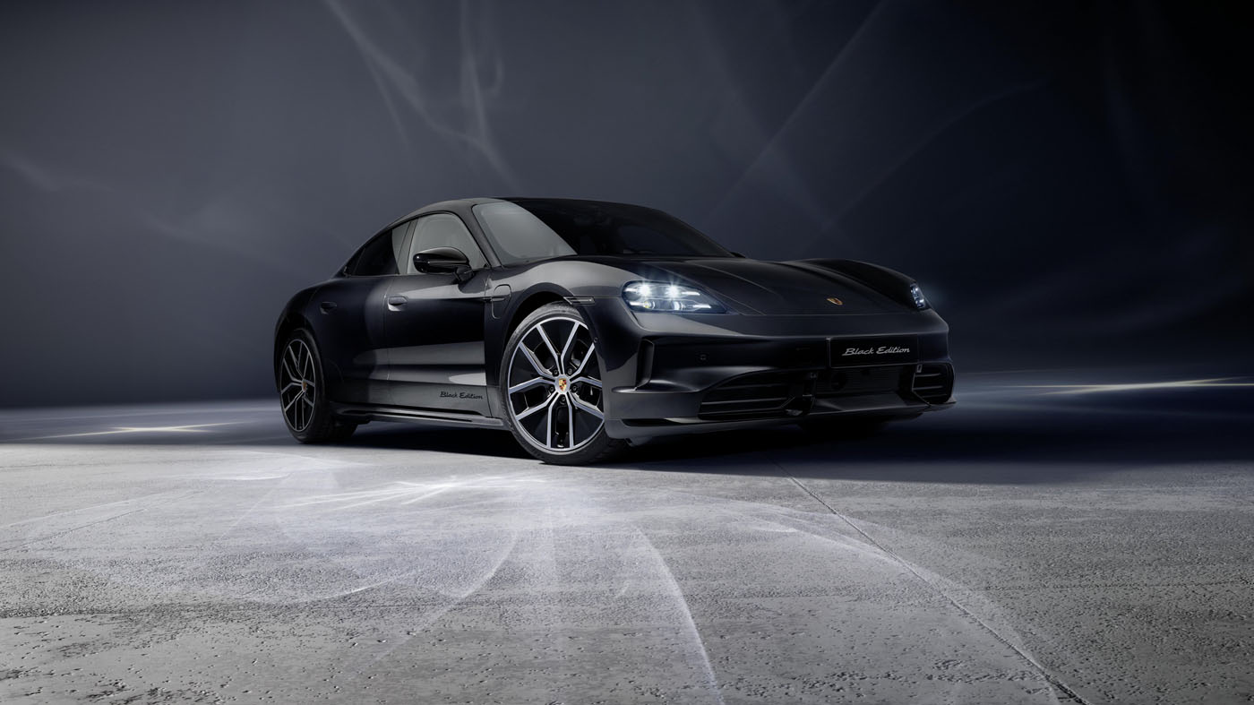 A 2026 Taycan Black Edition Porsche sports car is parked on a smooth, light-gray surface with a dark, gradient background.