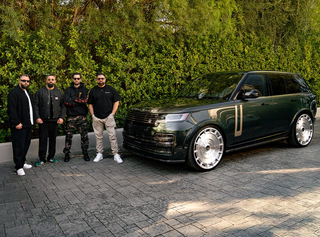 Four people stand next to a sleek black Range Rover L460 on a paved driveway, with lush greenery in the background.