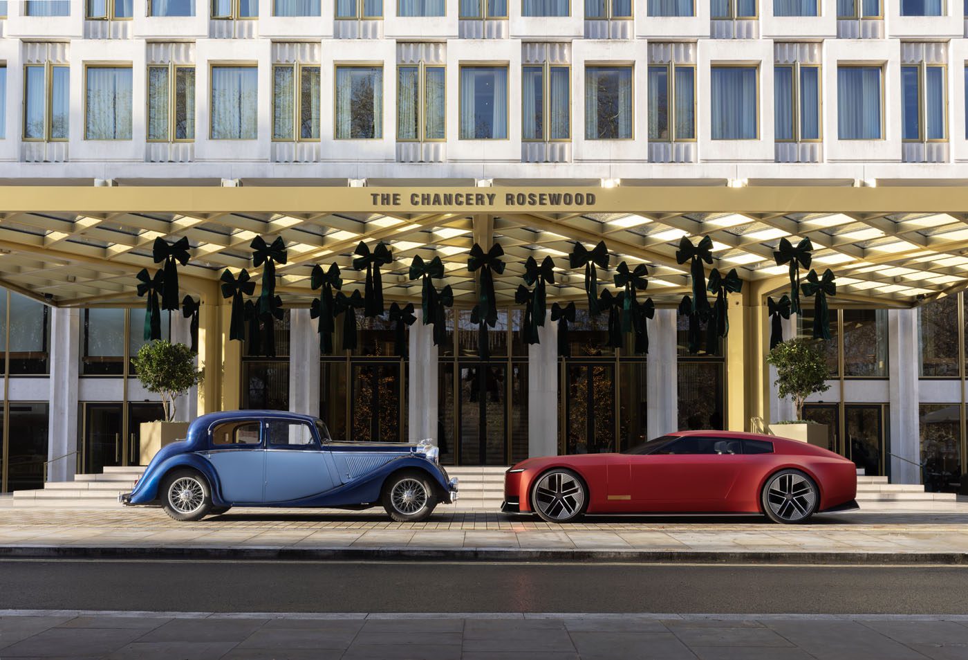 A vintage blue car and a modern red car are parked side by side in front of The Chancery Rosewood hotel building.