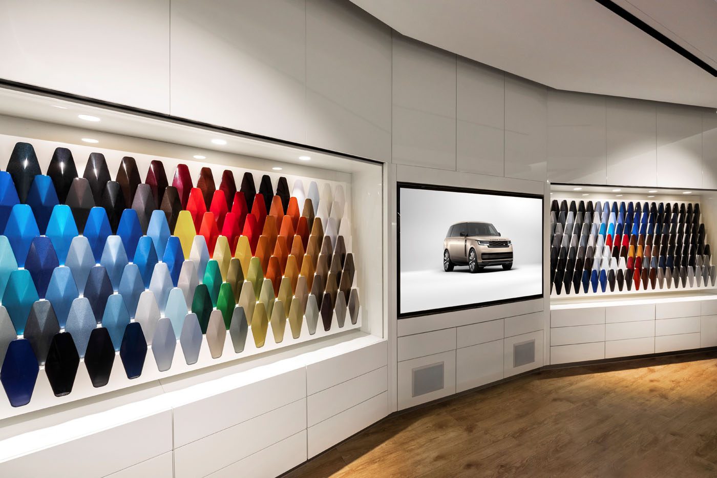 The showroom wall showcases an array of vibrant car paint samples, highlighted by a screen featuring an SUV image. Jaguar Land Rover invests $81.2M to expand paint facilities, reflecting their commitment to innovation and quality in every hue.