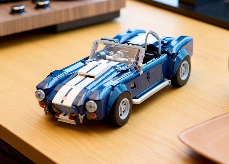A blue and white LEGO Shelby Cobra 427 model car, resembling a classic sports convertible, sits on a light wooden table—a striking build set for car enthusiasts and collectors.