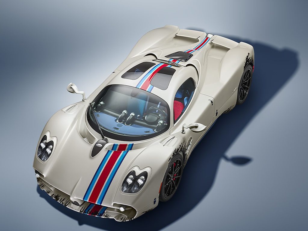 A white sports car with blue and red racing stripes, two seats, and aerodynamic design, photographed from above on a neutral background.