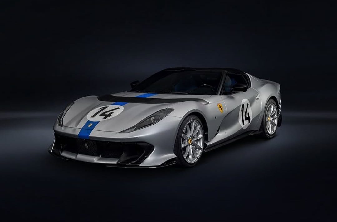 A gray Ferrari 812 Competizione with blue racing stripes and the number 14 on its hood and sides, tailor-made for speed, is set against a dark background.