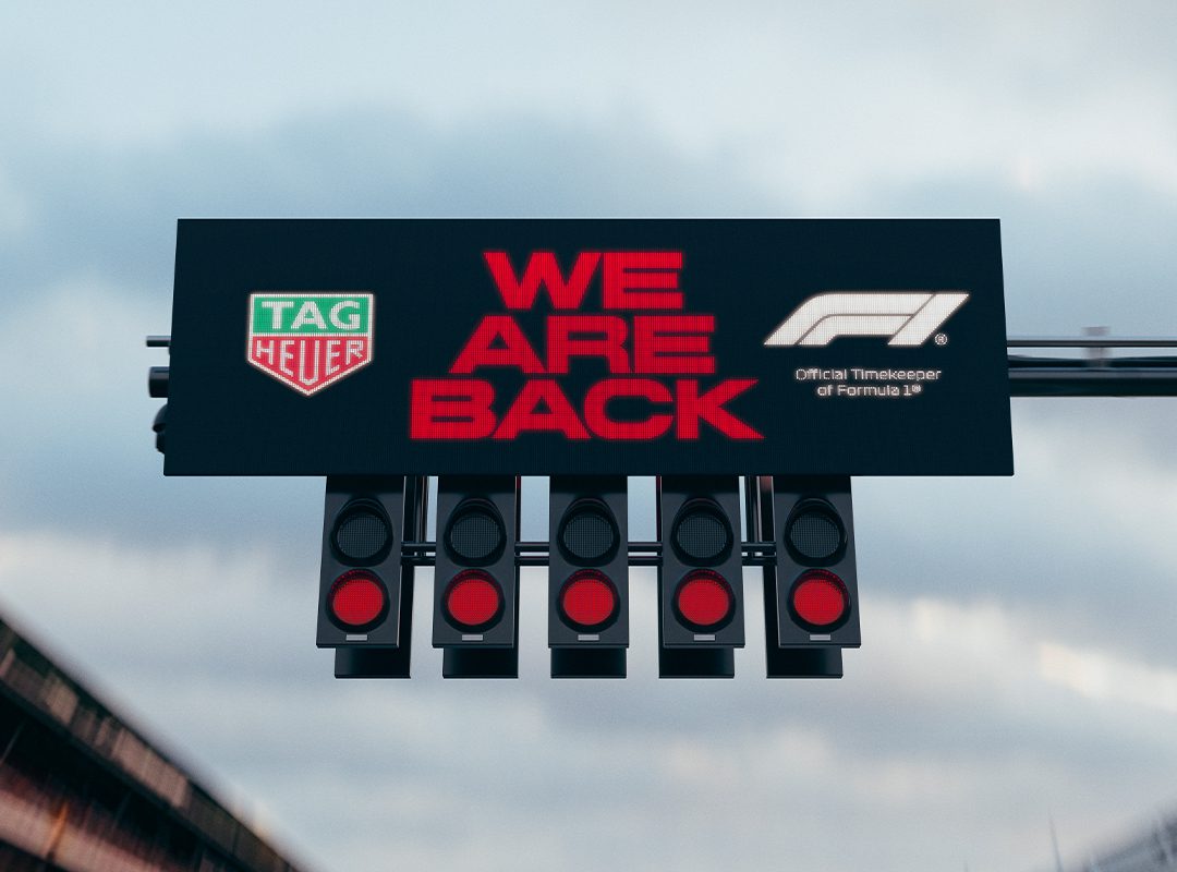 A Formula 1 starting light proudly flashes "WE ARE BACK," accompanied by the iconic TAG Heuer emblem, celebrating its role as the Official Timekeeper alongside the F1 logo.