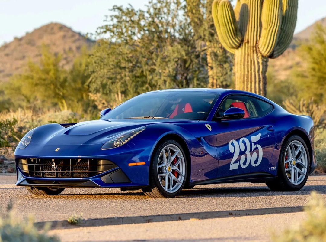 A blue Ferrari F12berlinetta, a true example of Ferrari supercars, with the number 235 on the door, is parked on a road in a desert landscape surrounded by cacti and mountains.