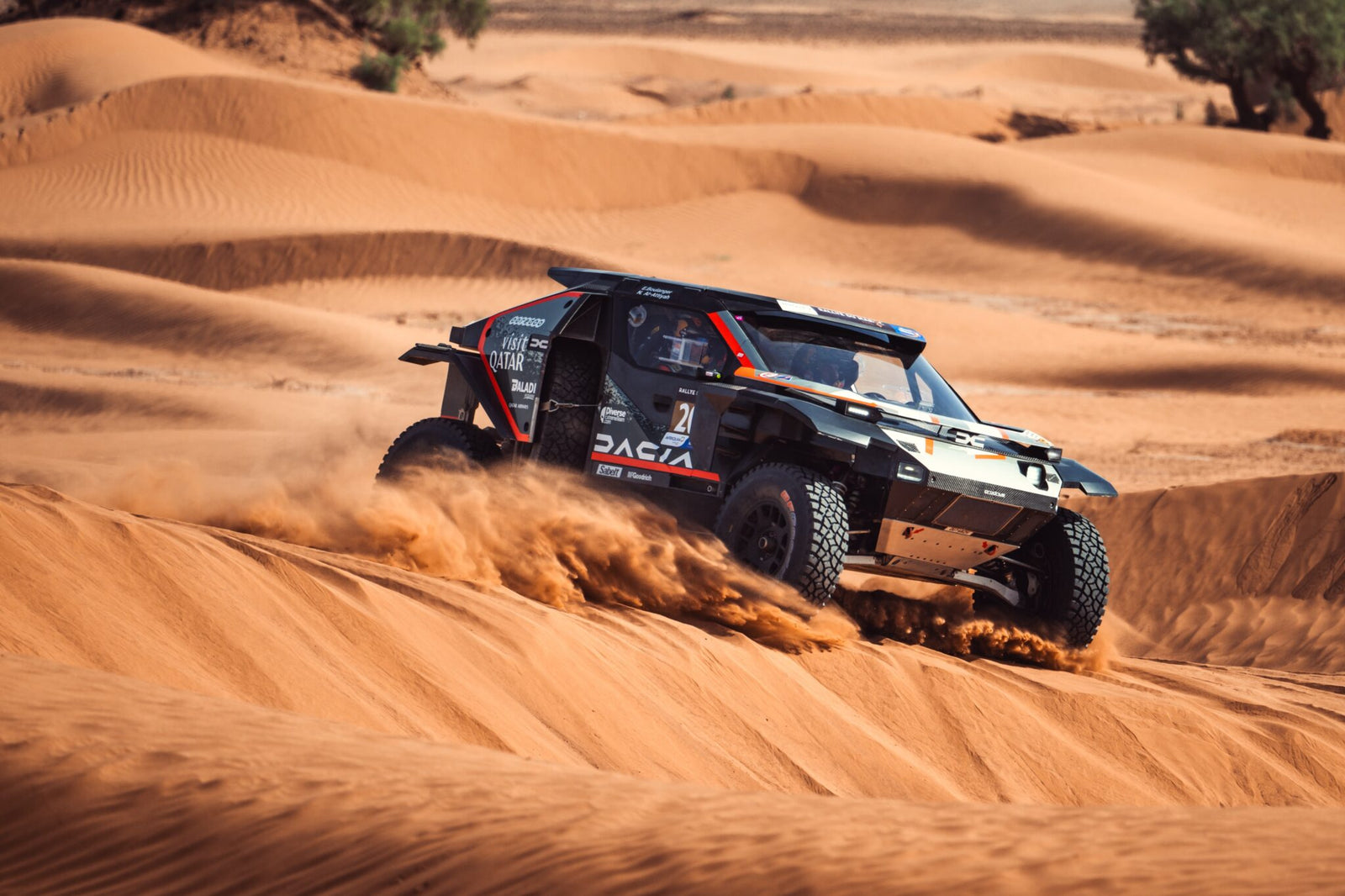 A dune buggy from Dacia Sandriders races across sand dunes, kicking up clouds of dust under a clear sky, reminiscent of the thrilling Dakar Rally 2025.