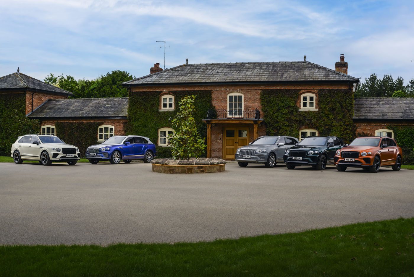Six cars, including a sleek Bentley, are parked in front of a brick house with ivy-covered walls and a paved driveway. The setting evokes the sophistication of The Mews and promises a refined client experience.
